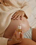 Pregnant person holding a bottle of oil against their belly.