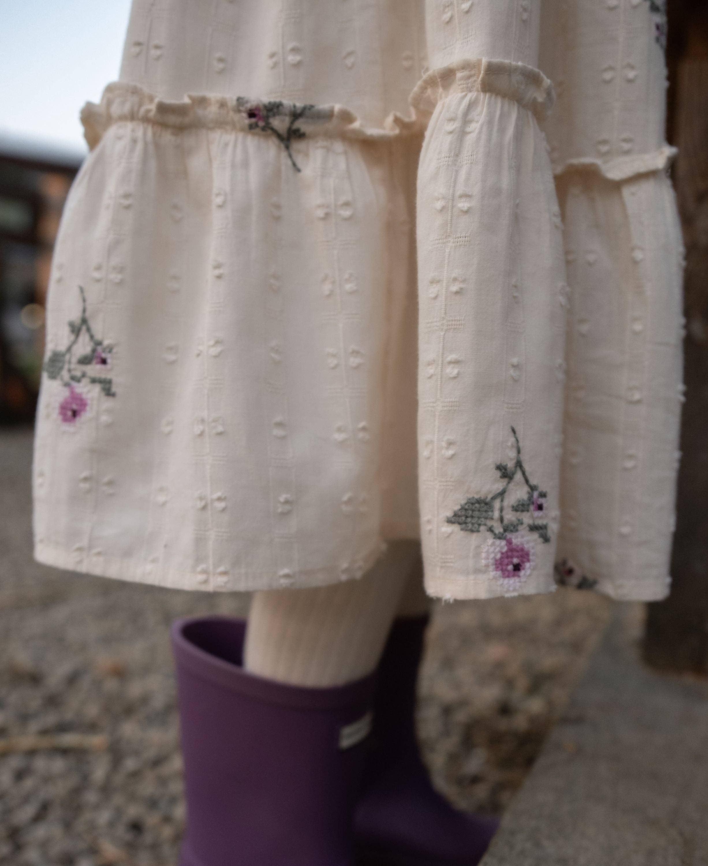 White embroidered dress with floral patterns and purple rain boots on a blurred background
