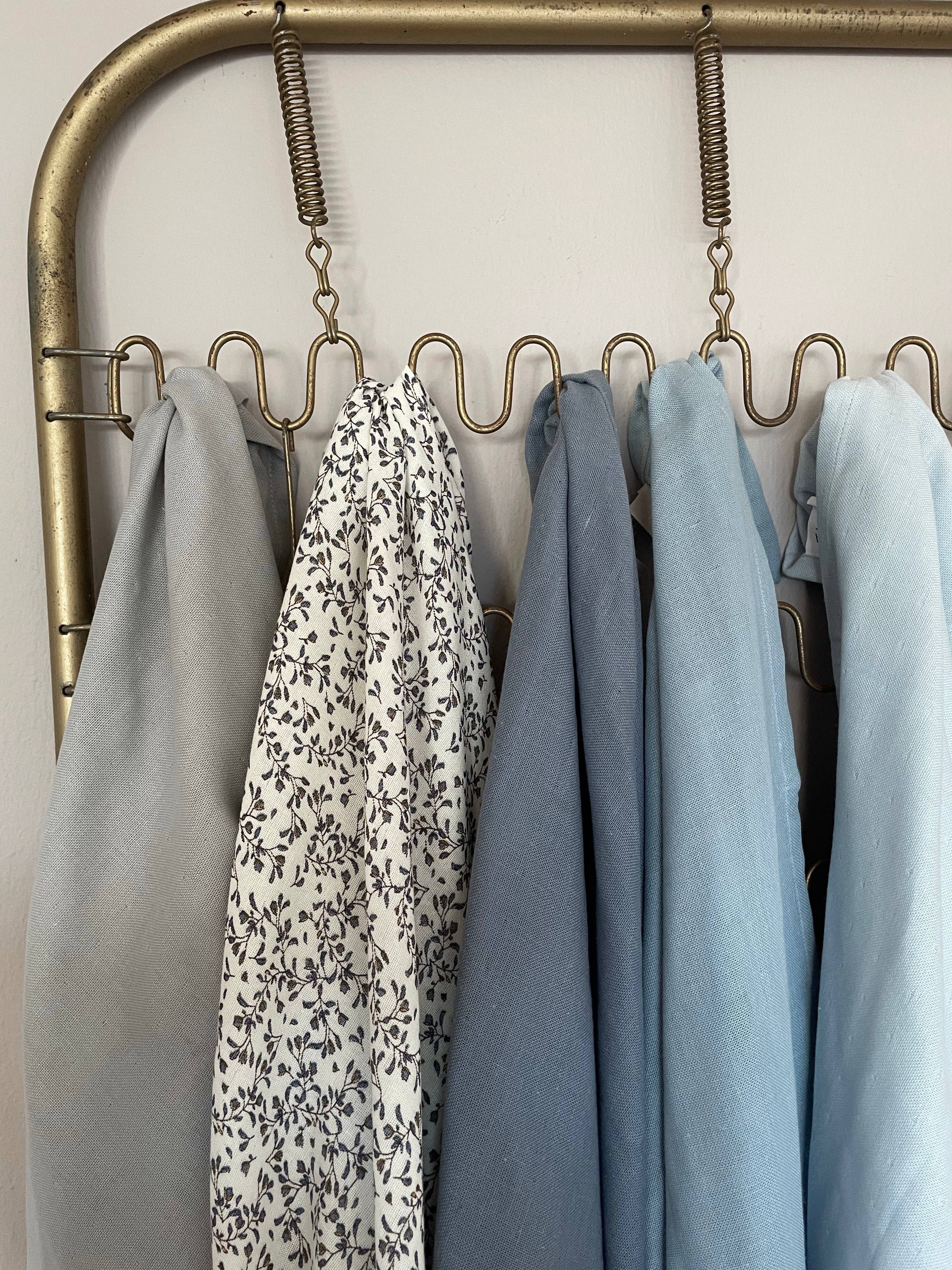 A close-up of a brass garment rack with multiple hooks holding several light blue and white patterned fabrics.