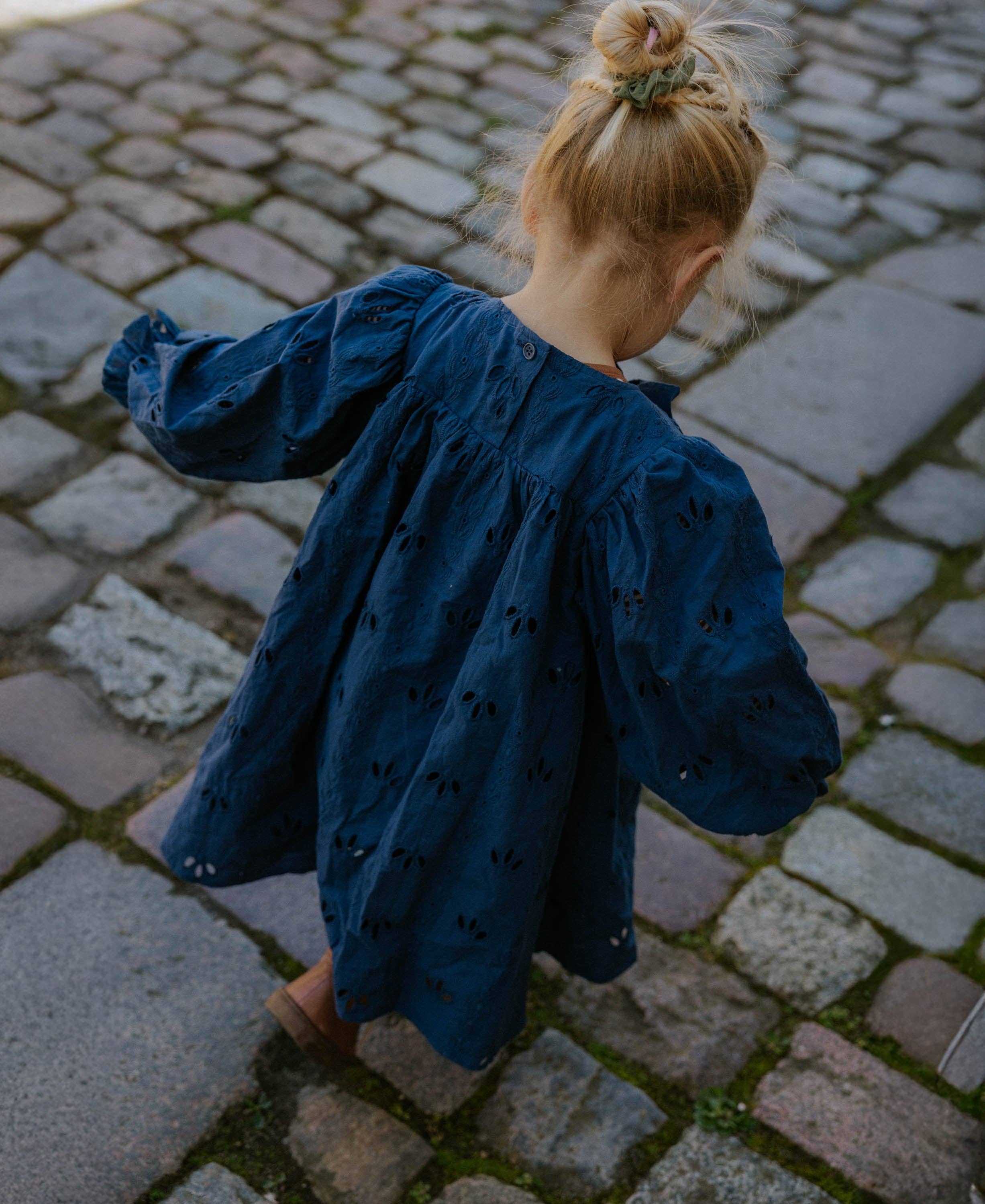 Child in a blue dress walking on a cobblestone street