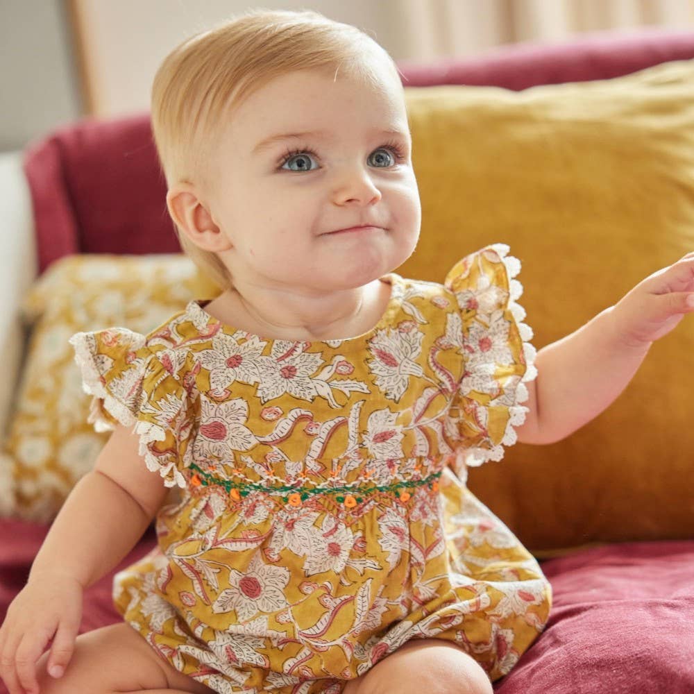 Baby in a floral dress sitting on a couch