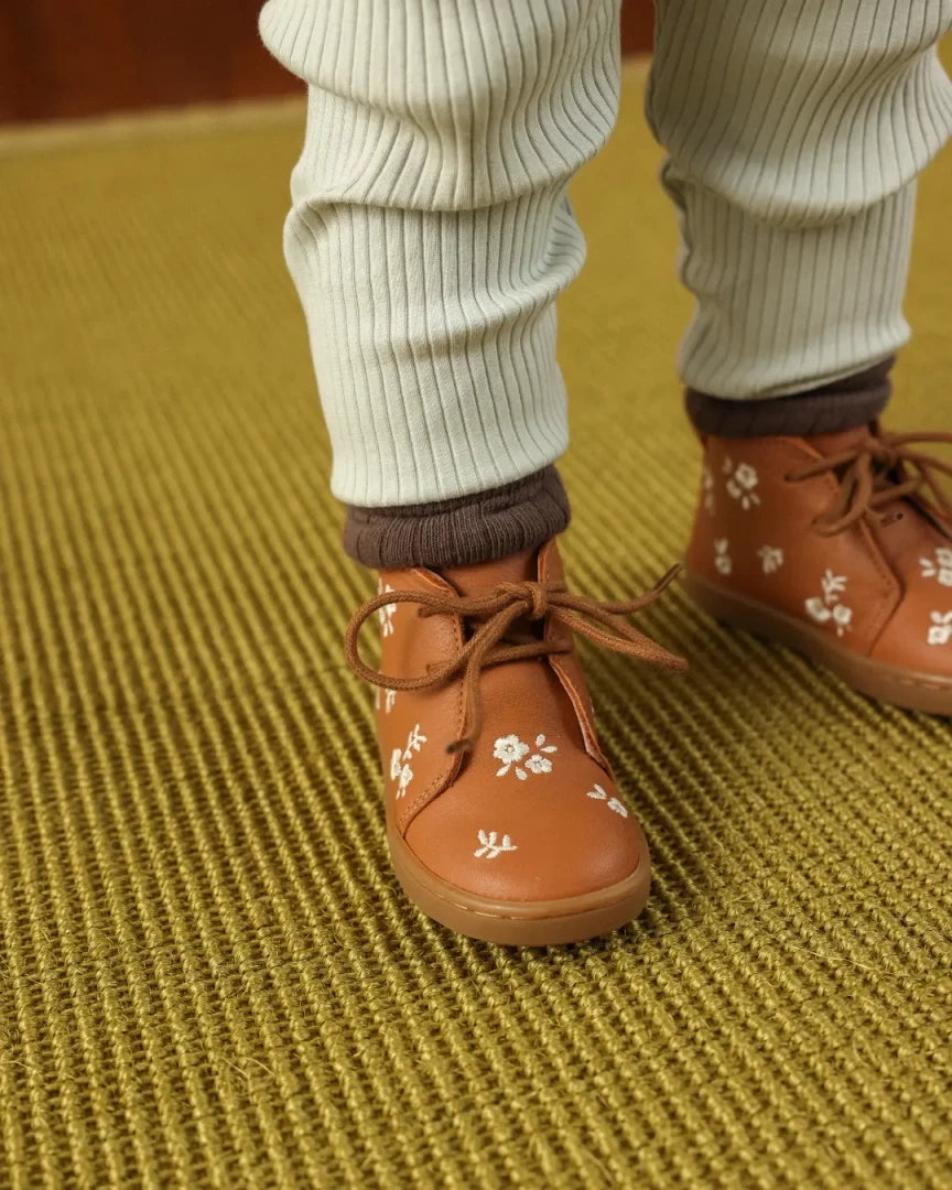 Brown shoes with floral patterns worn by a person on a textured green floor.