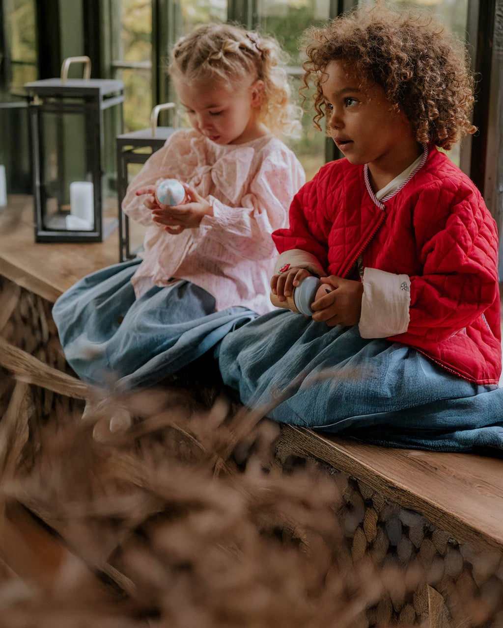 Two children sitting on a wooden bench holding small objects, with a blurred background.