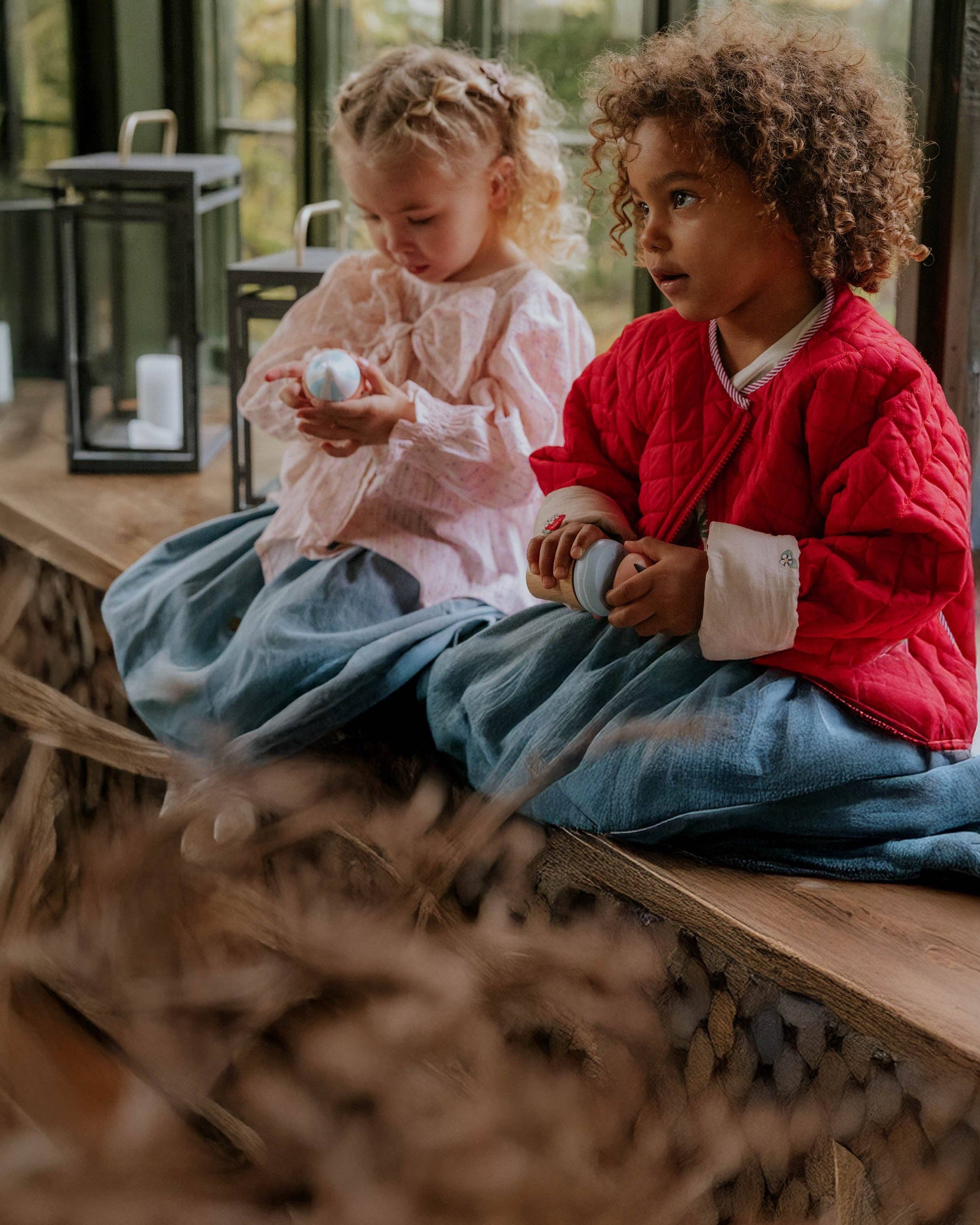 Two children sitting on a wooden bench holding small objects, with a blurred background.