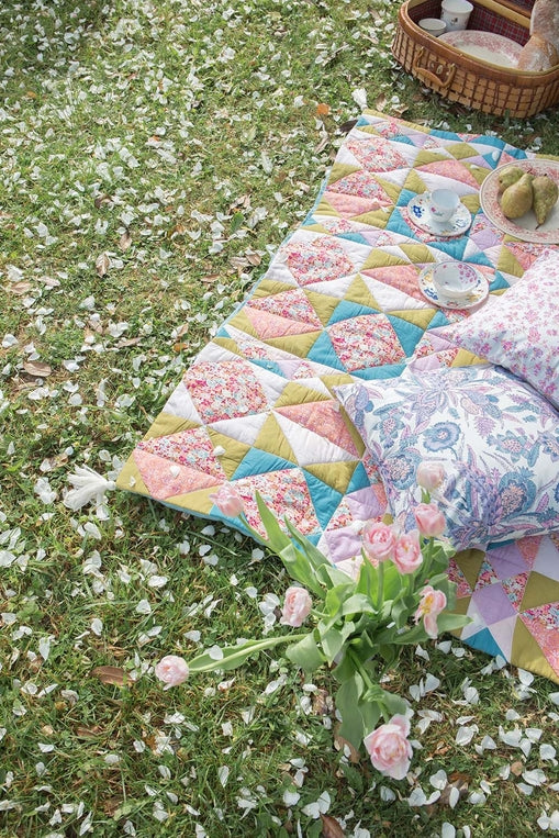 Colorful quilt on grass with flowers and a basket