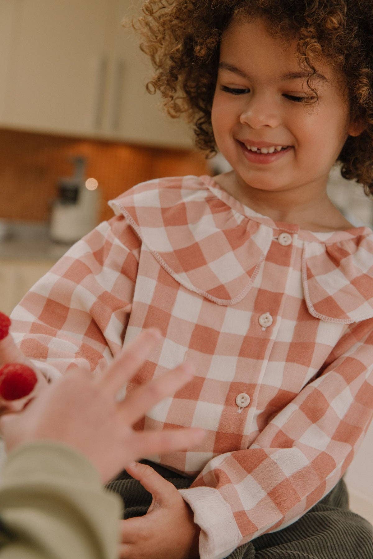 Child wearing a pink and white checkered shirt in a kitchen setting