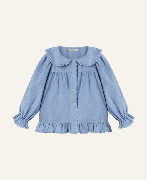 A light blue long-sleeve blouse for toddlers, featuring a large Peter Pan collar, button-up front, and ruffled trim at the hem and cuffs, shown flat on a light gray background.