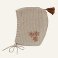 Knitted bonnet with floral details and a brown tassel on a white background