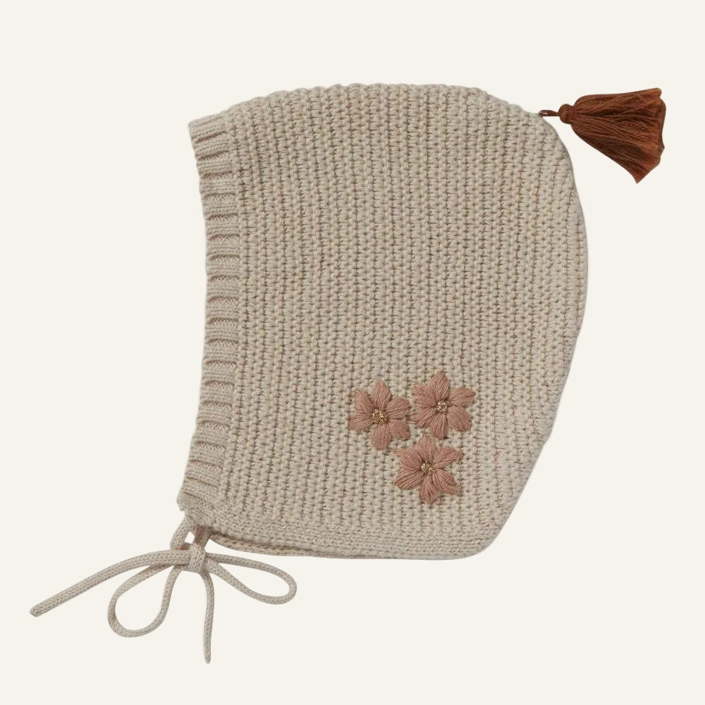Knitted bonnet with floral details and a brown tassel on a white background