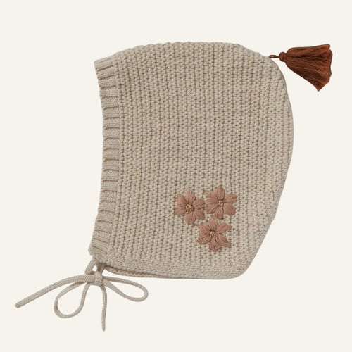 Knitted bonnet with floral details and a brown tassel on a white background
