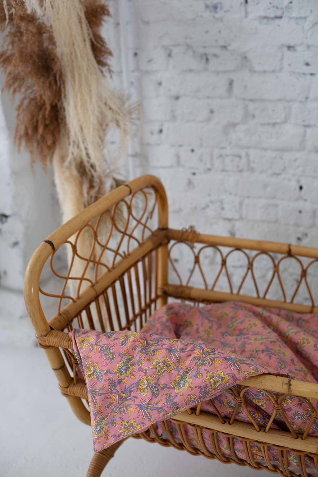 Wicker crib with pink floral blanket against a white brick wall