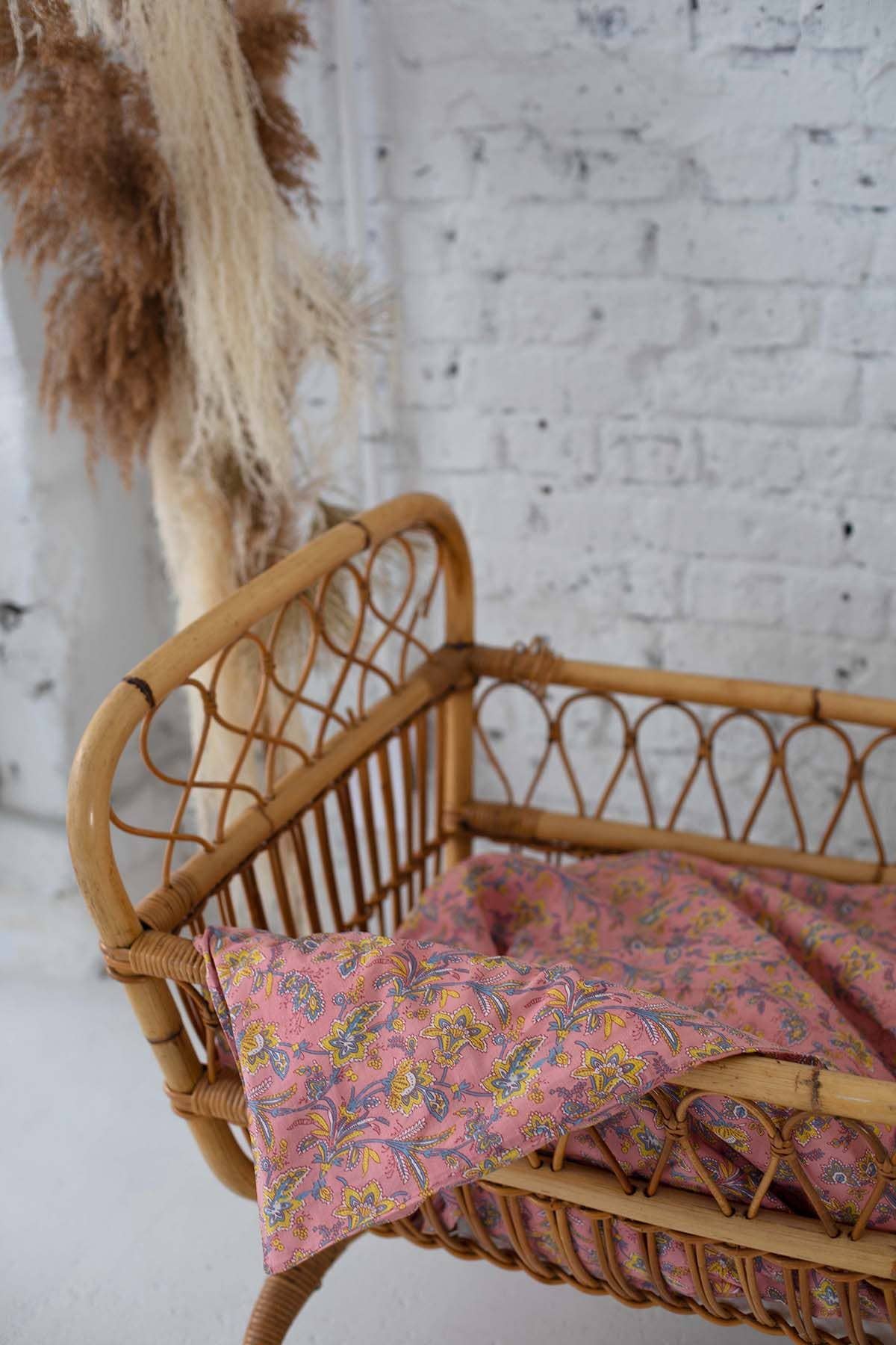 Wicker crib with pink floral blanket against a white brick wall