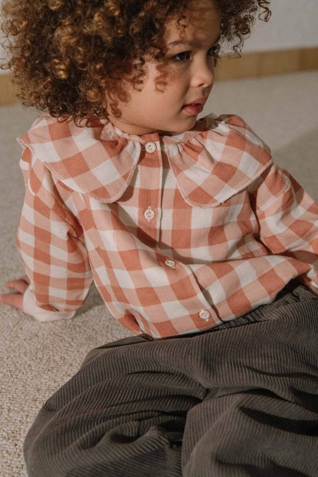 Child wearing a checkered shirt sitting on the floor