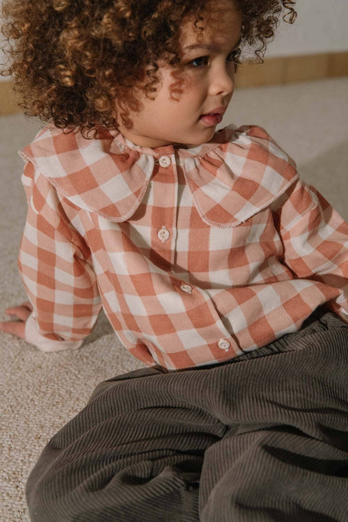 Child wearing a checkered shirt sitting on the floor