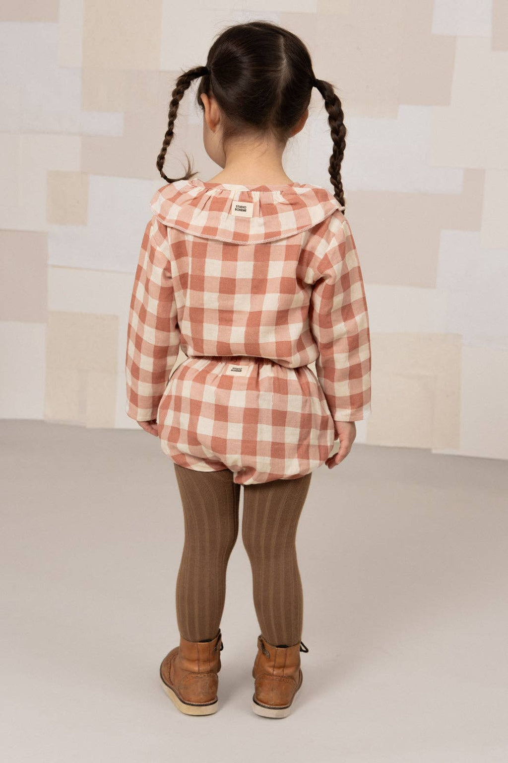 Child wearing a pink checkered outfit with a neutral background