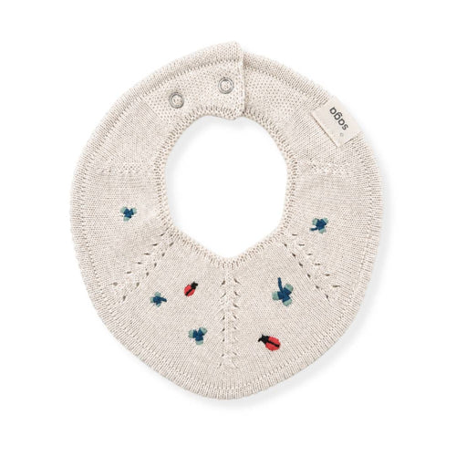An off-white knitted baby bib with embroidered ladybugs and bees in red and blue, featuring a small brand tag that reads 'sodas'.