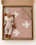 A baby gift set in a kraft paper box, featuring a dusty pink knit blanket with white bird patterns and a plush toy dressed as a deer in beige and brown striped clothing.