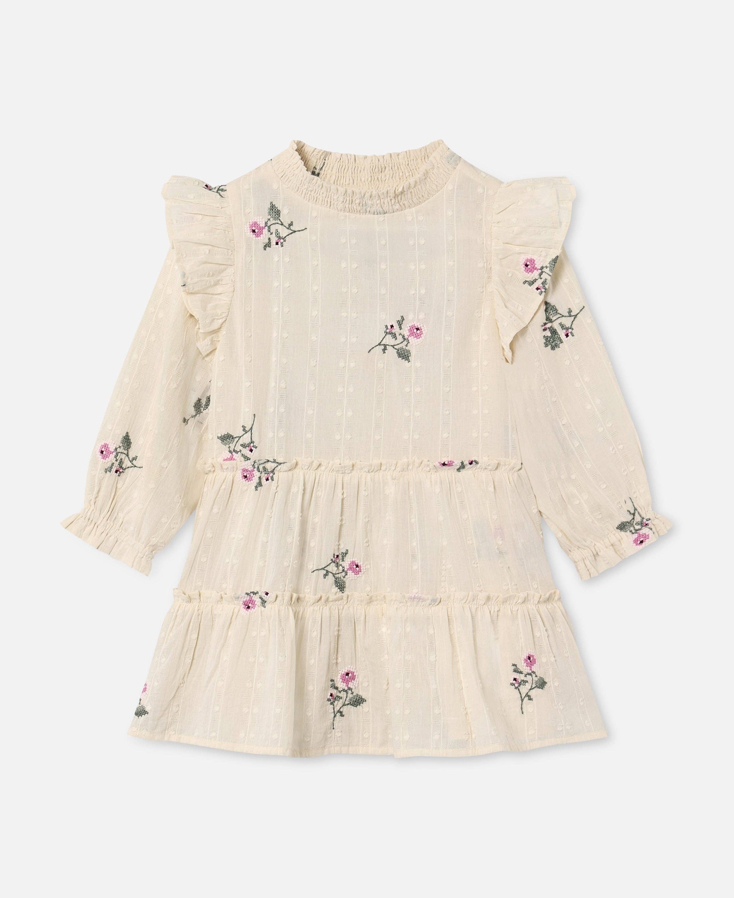 A cream-colored long-sleeve baby dress with ruffled shoulders, a smocked neck, and a tiered skirt, decorated with small pink and green floral prints.