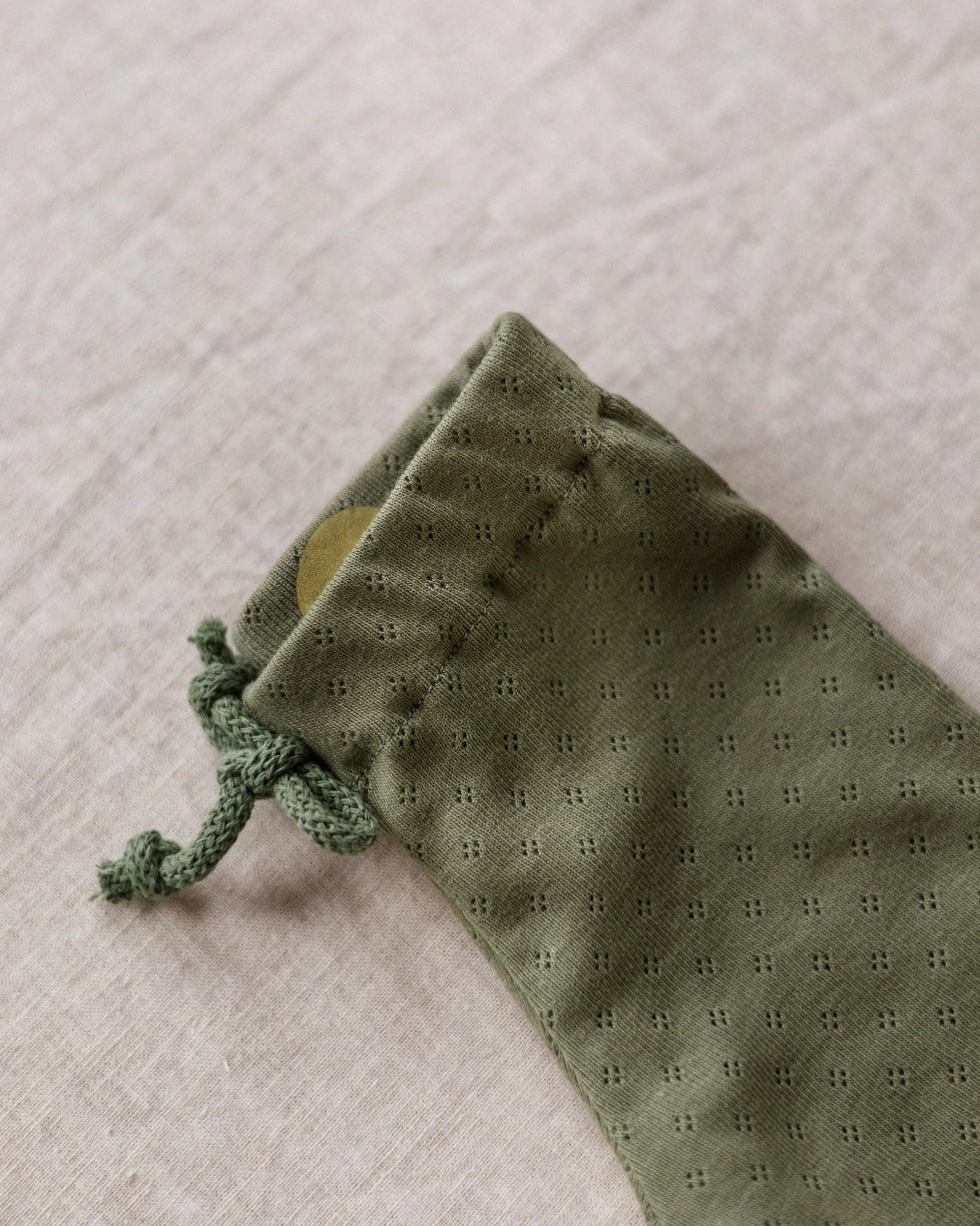 An olive green drawstring pouch with a small eyelet pattern, shown on a textured beige linen background.
