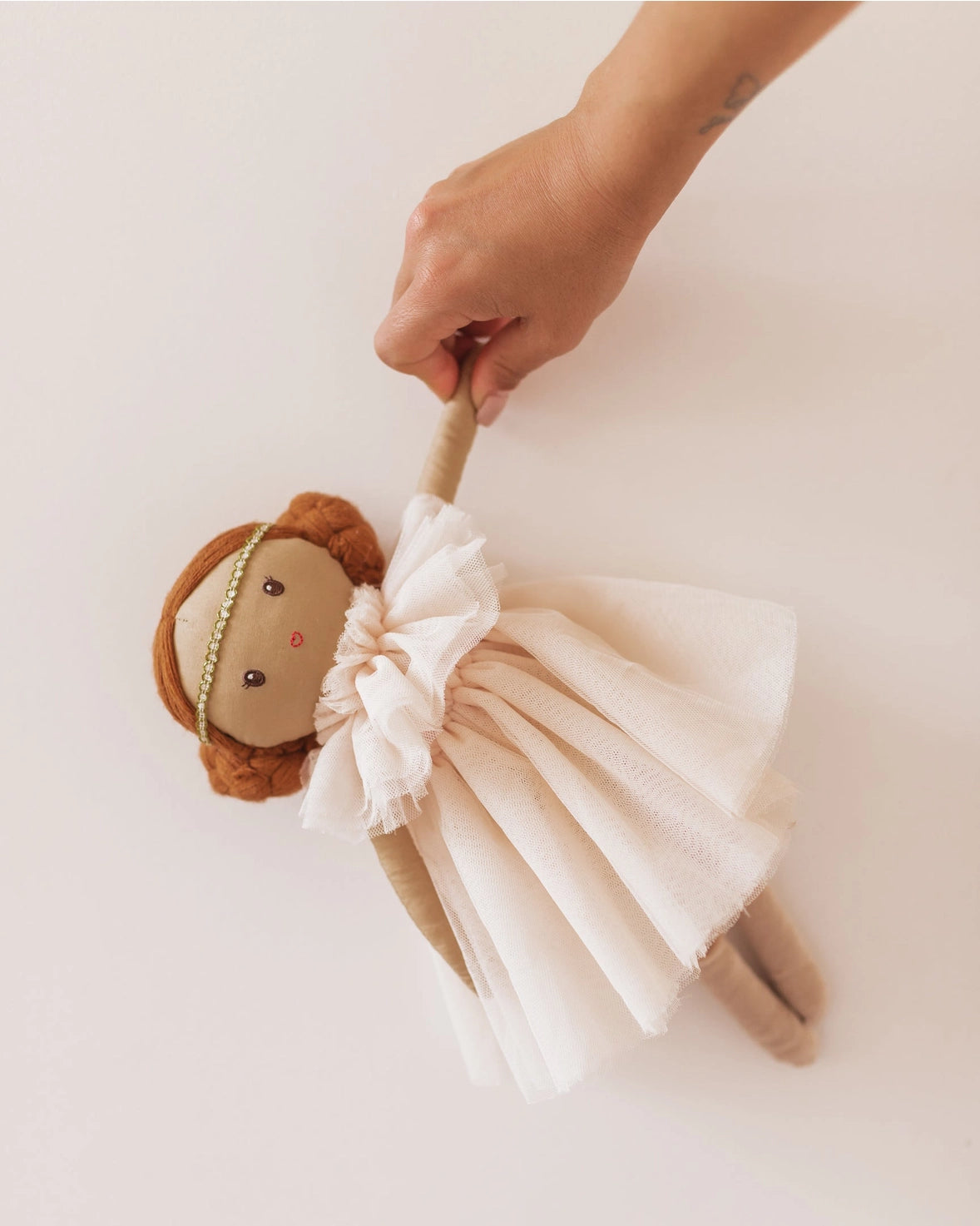 Hand holding a plush toy lion with a white tulle skirt on a light background