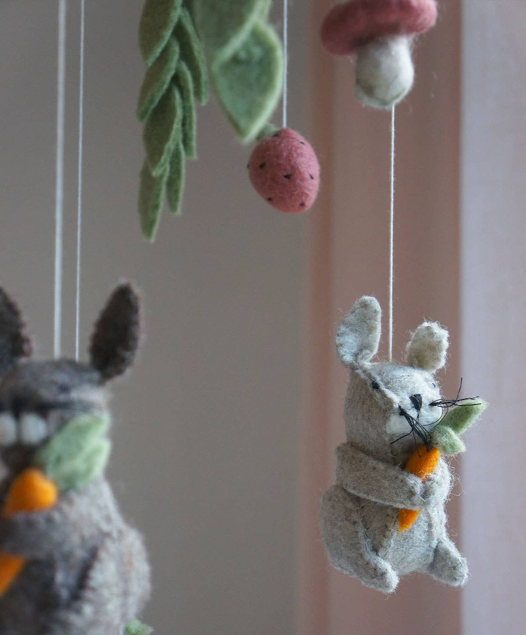 Felt animal toys hanging from strings against a neutral background