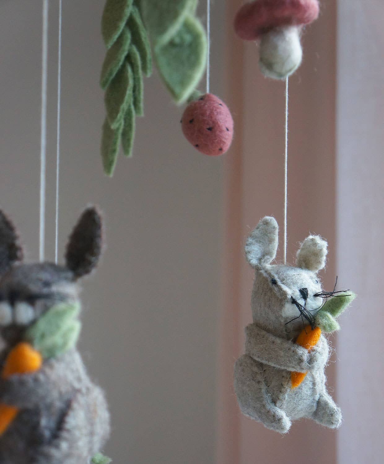 Felt animal toys hanging from strings against a neutral background