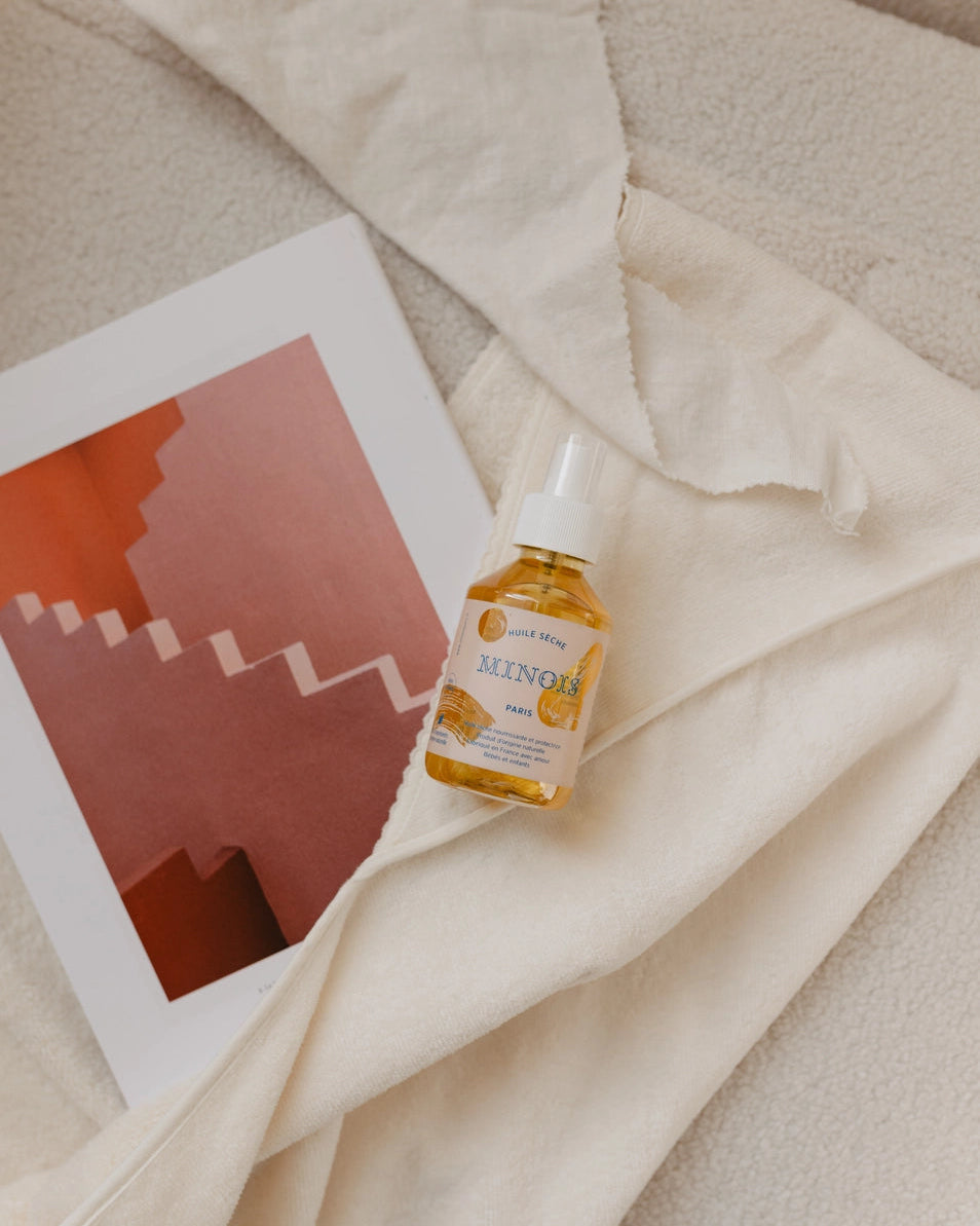 Small bottle of dry oil on a textured surface with a framed abstract artwork.