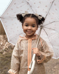 Child holding a transparent umbrella with floral patterns, wearing a beige raincoat.