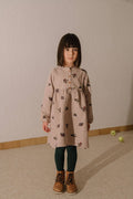 Young girl wearing a patterned dress standing against a plain wall.