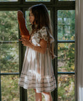 Young girl holding a baguette in front of a window with a view of trees.