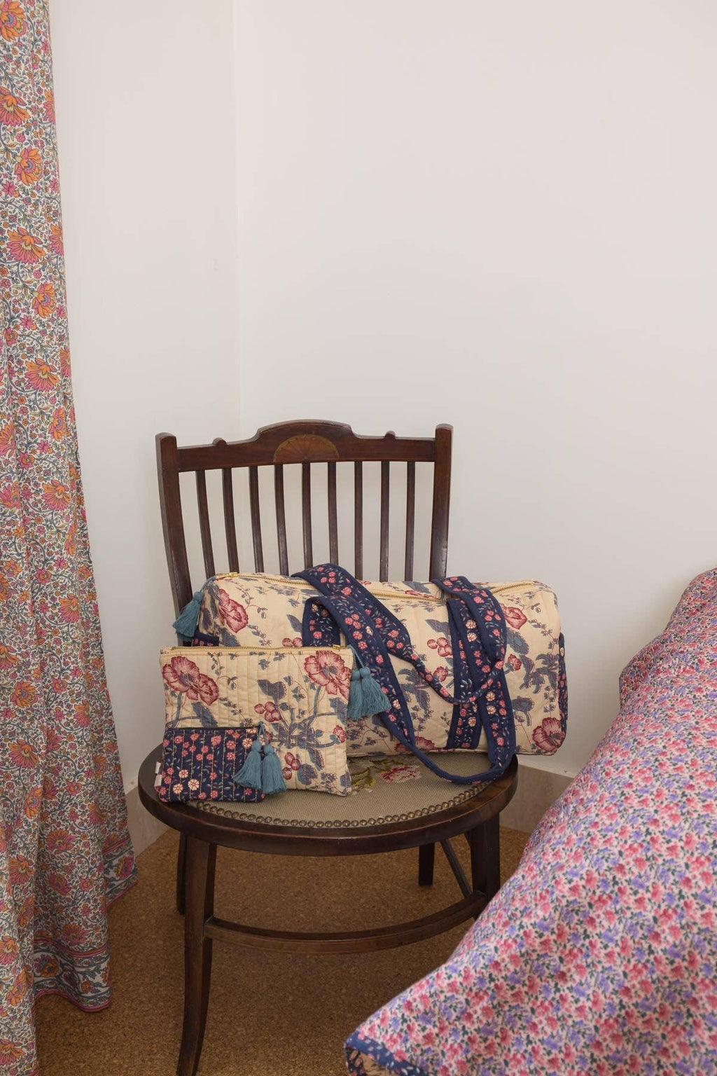 Floral-patterned bags on a wooden chair against a white wall with a curtain on the left.