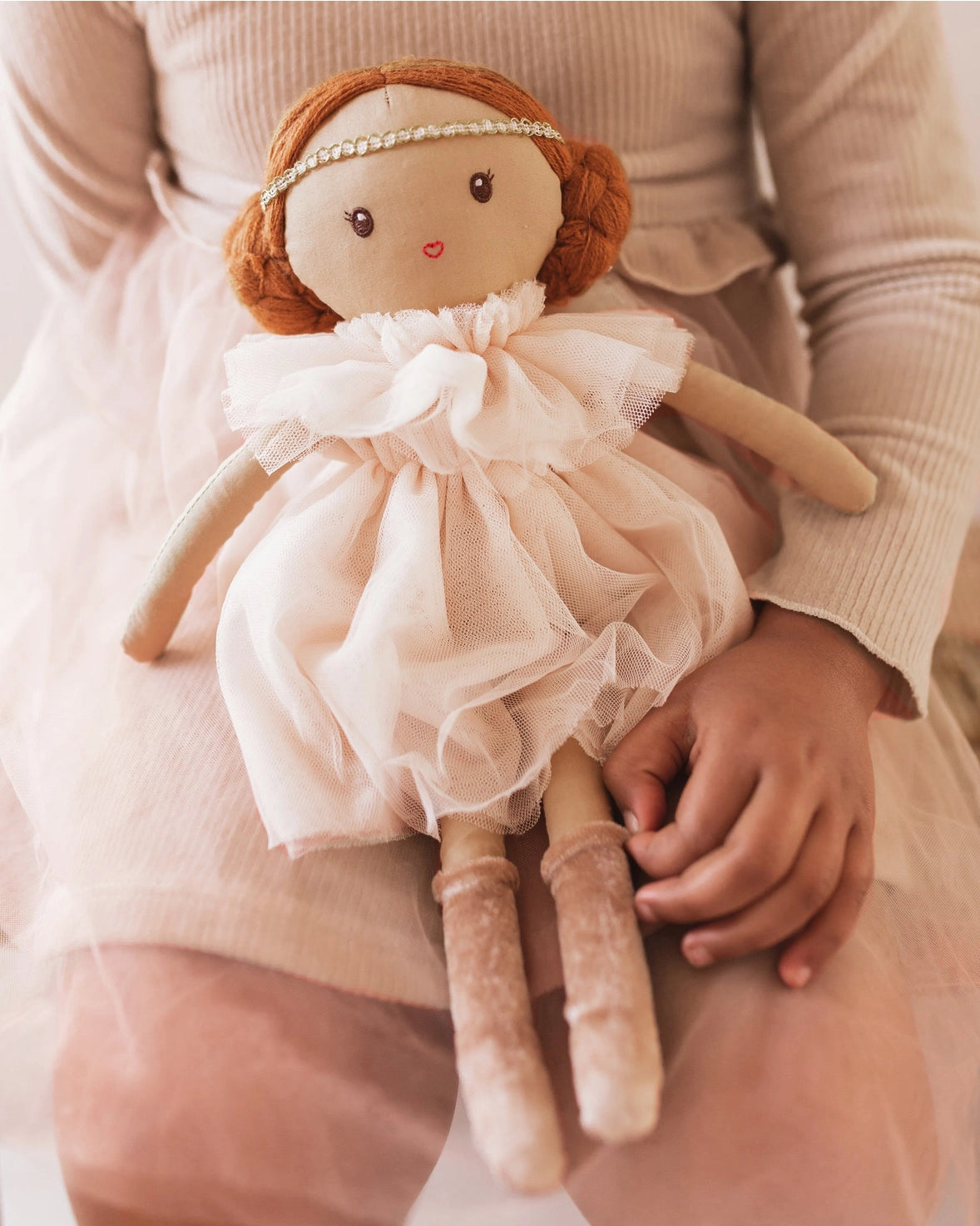 Hand holding a small doll with a delicate dress and red hair.