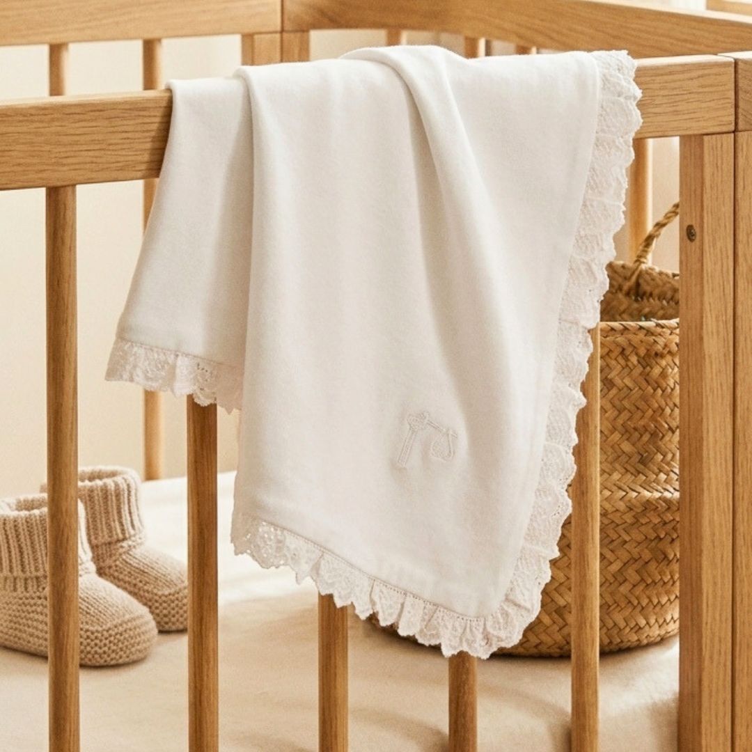 White lace-trimmed blanket draped over a wooden crib with beige boots and a woven basket in the background.