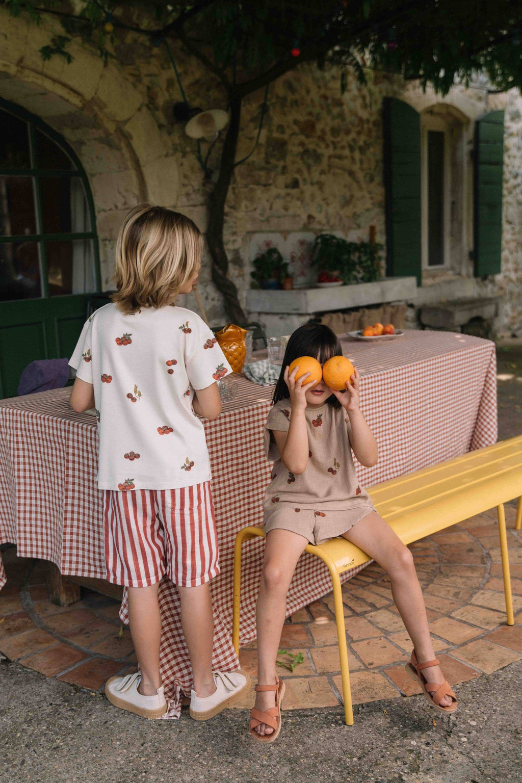 Two children playing with oranges in a garden setting.