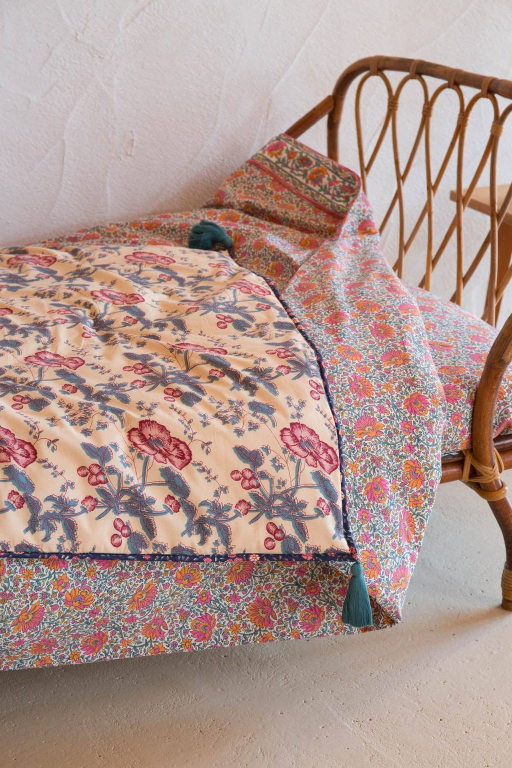 Floral quilt draped over a wicker chair against a white wall.