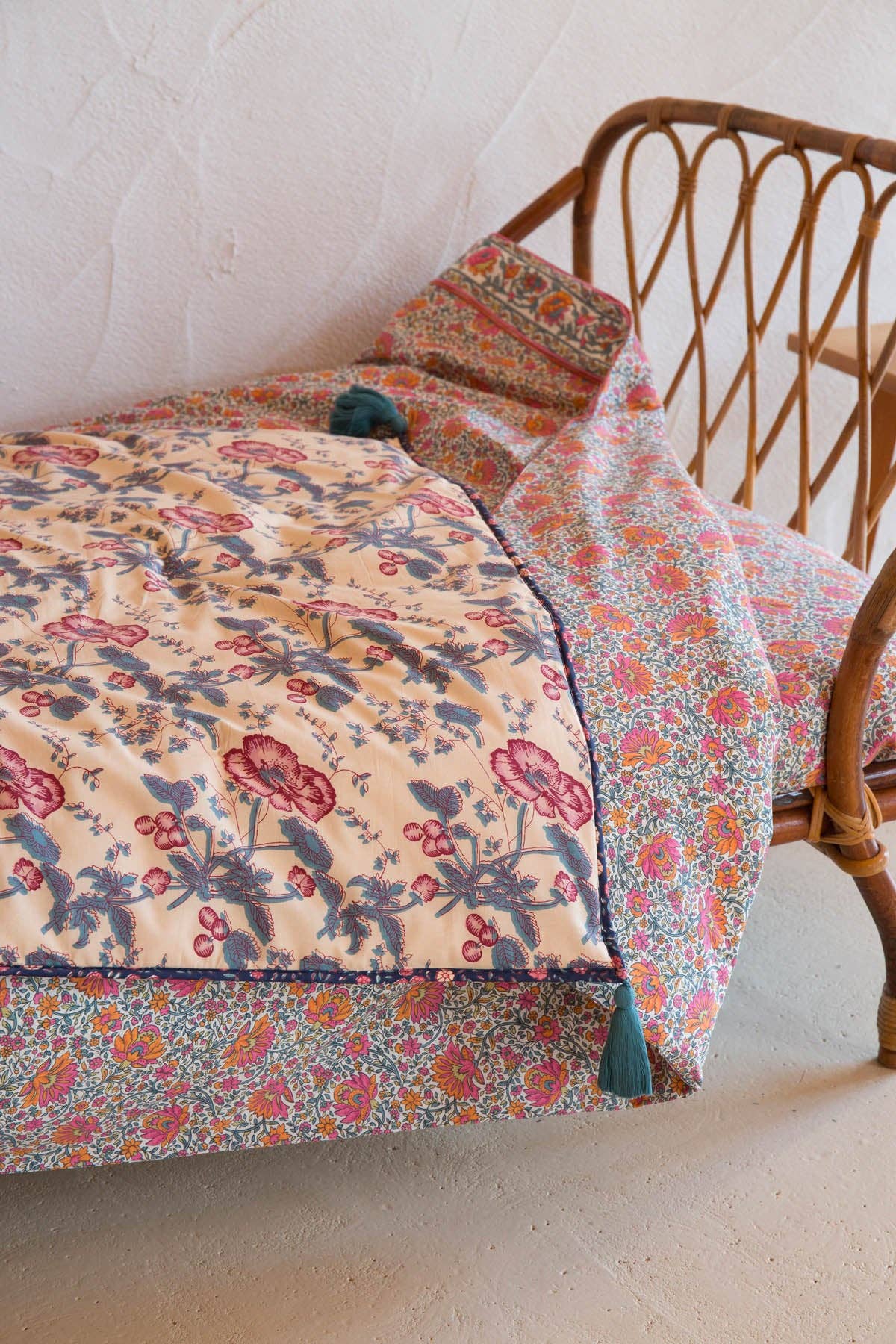 Floral quilt draped over a wicker chair against a white wall.