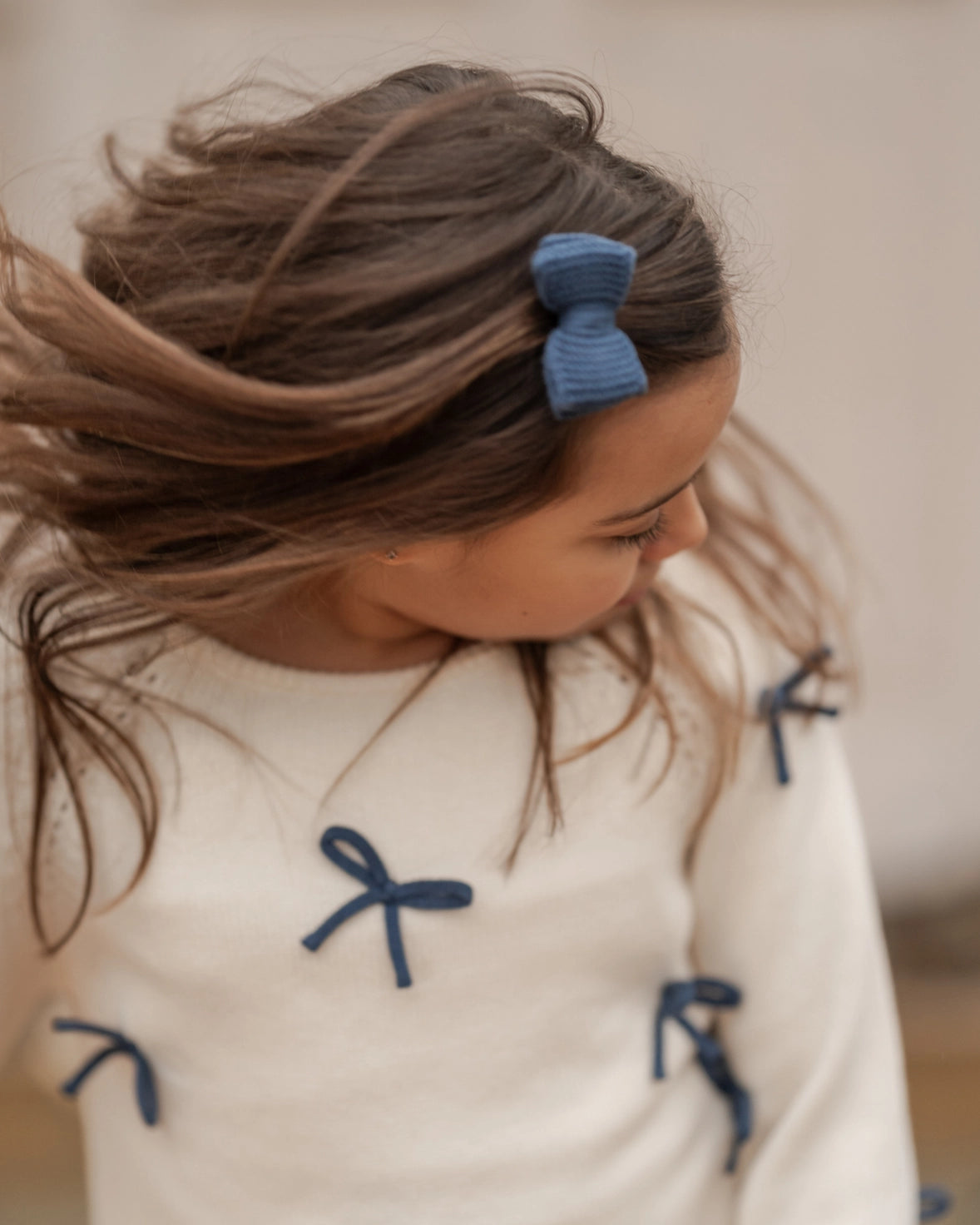 Person wearing a white sweater with blue bows and a blue hair clip.